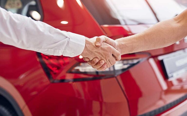 A man and woman discussing a vehicle while standing beside cars in a dealership parking lot.