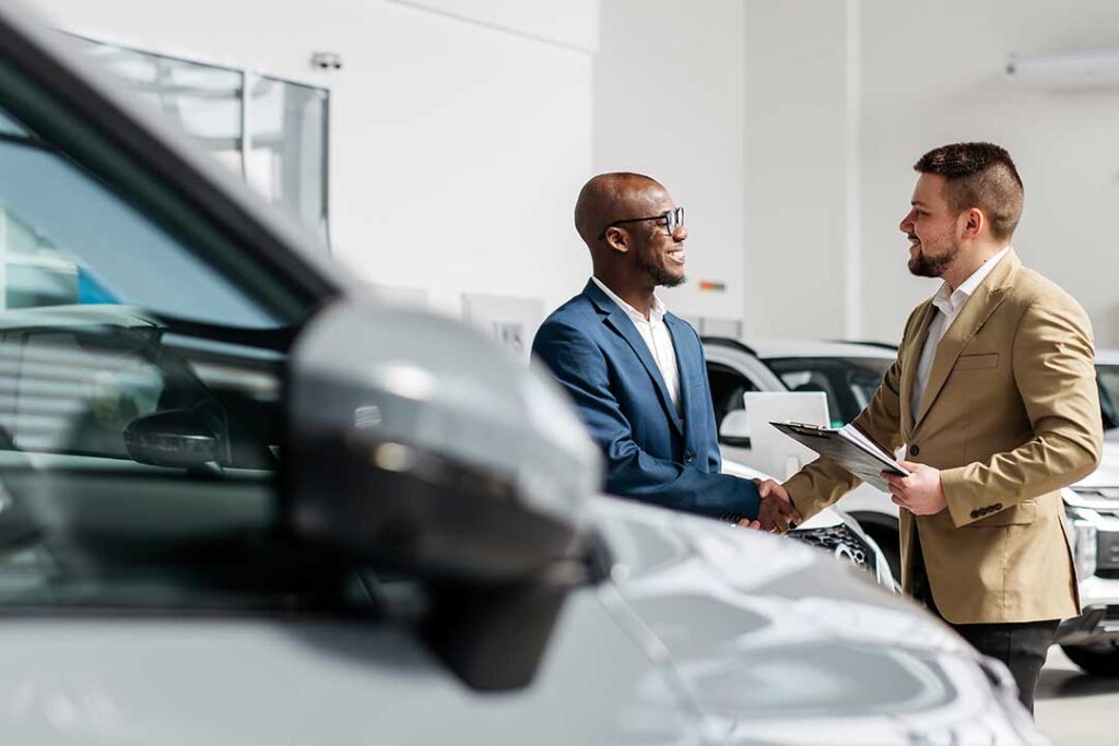 A person reviews car loan documents with a pen at a table, with car keys and a calculator nearby.