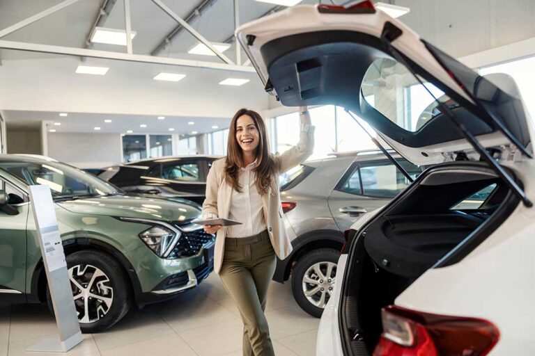 A car buyer and a salesperson review paperwork next to a vehicle in a dealership showroom.