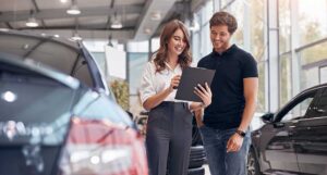 Person checking tire pressure beside a parked vehicle with an open hood and maintenance tools nearby
